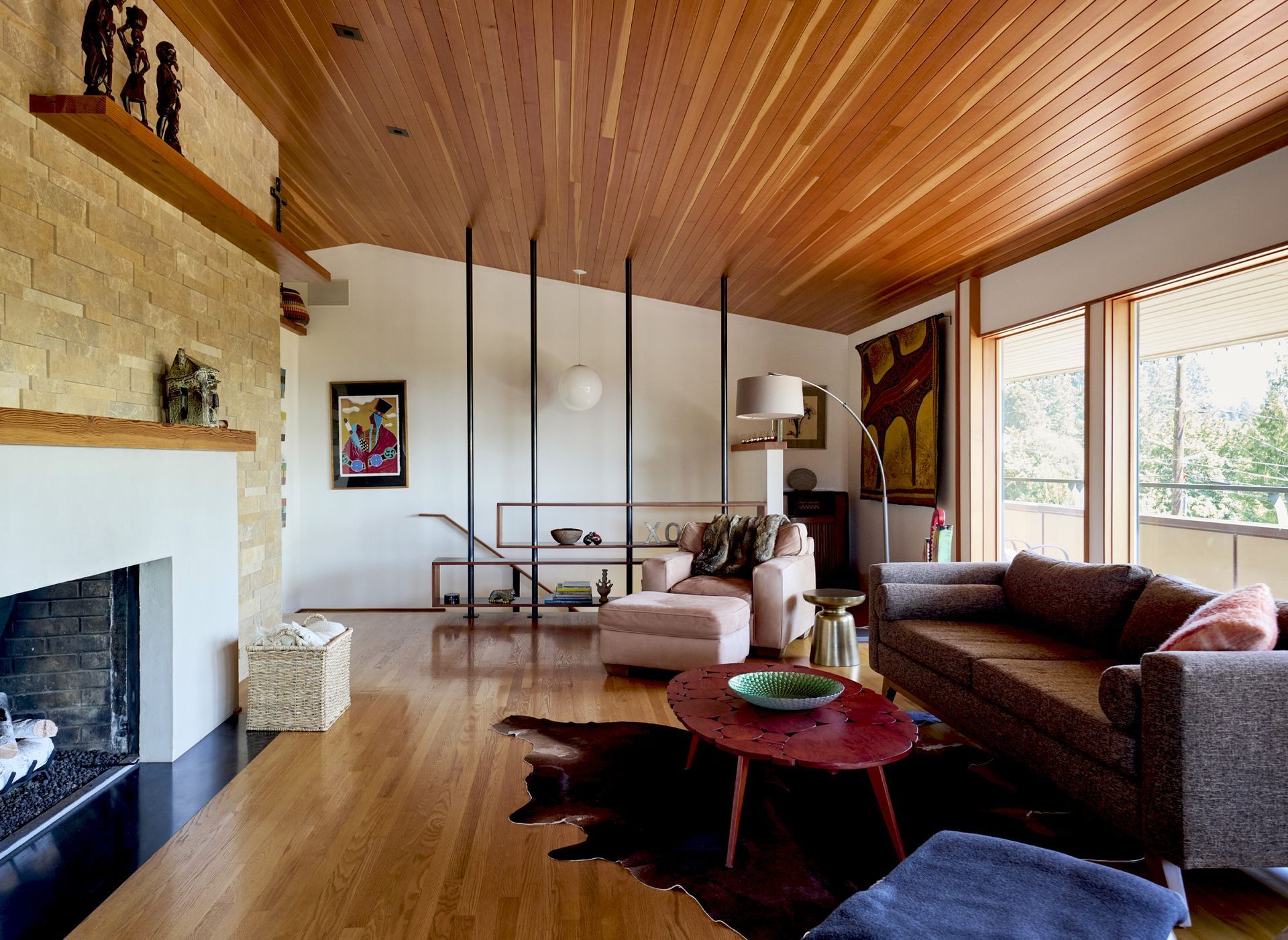 Wide view of the airy living room with new picture windows, a vaulted ceiling paneled in fir, a new fireplace and oak floors.
