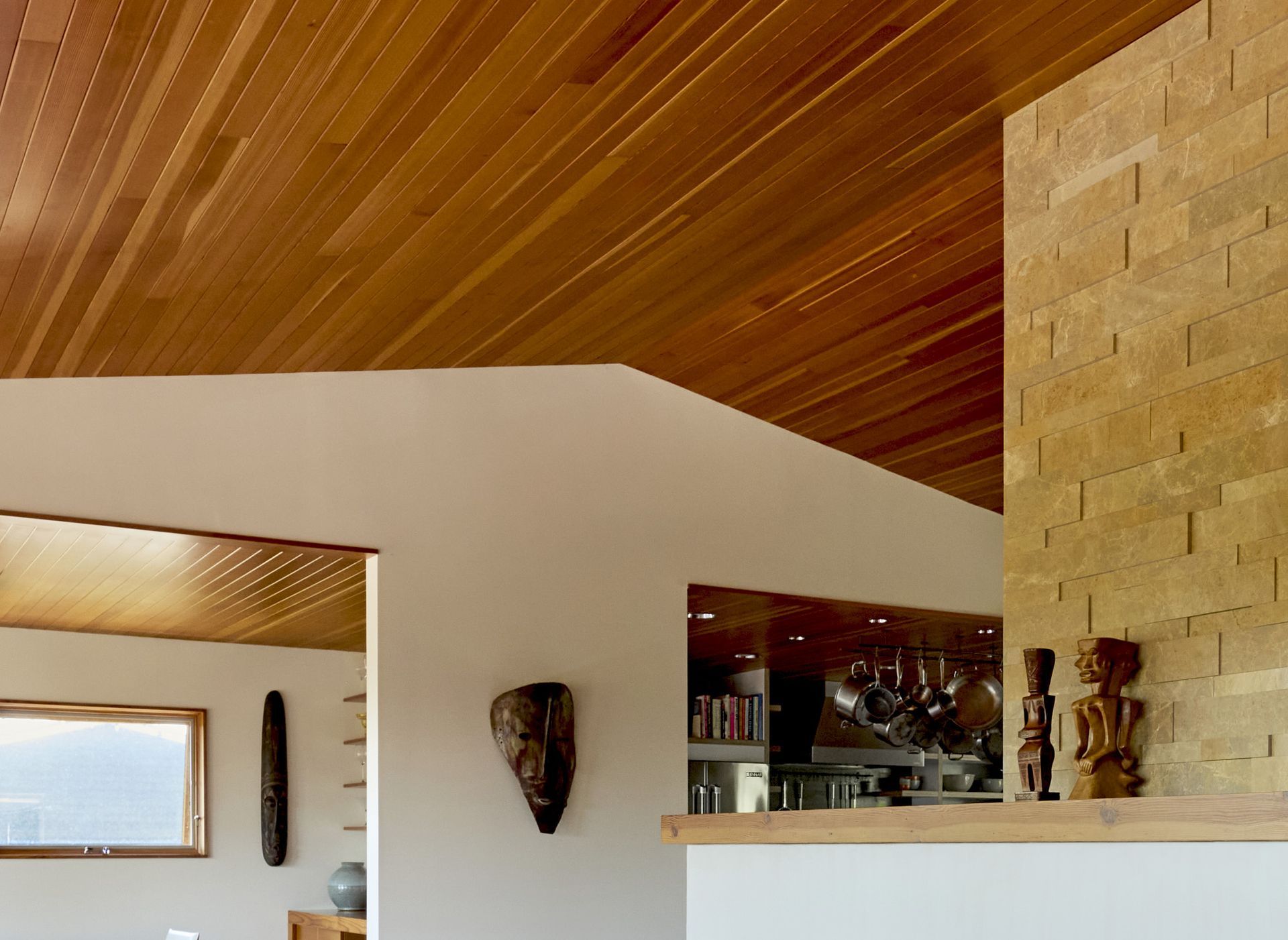 Closer view of the connection between the living room, dining room and kitchen with warm and inviting palette of materials: paneled fir ceiling, oak floors, and painted white walls accented by sculptural art work.
