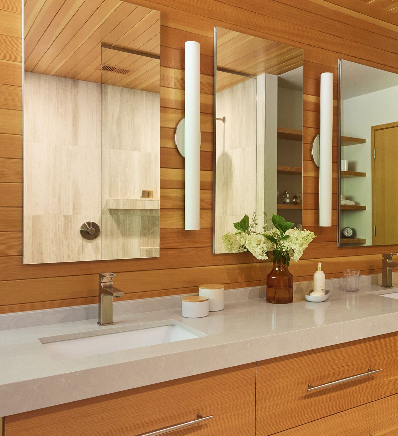 Close view of the sculptural, floating double vanity with a trio of mirrored medicine cabinets, plentiful lighting, undermounted sinks and elegant dove gray quartz countertop.