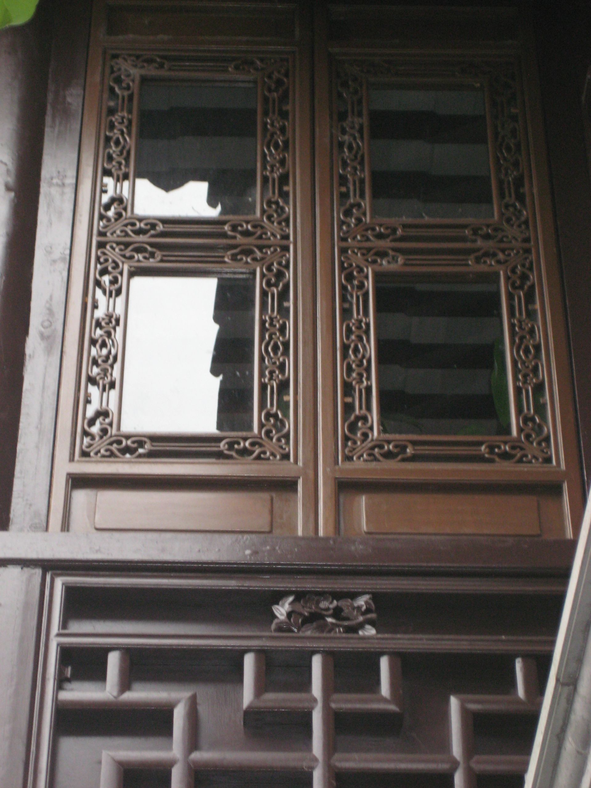 Ornate wooden window with carved lattice panels and dark glass on a building facade