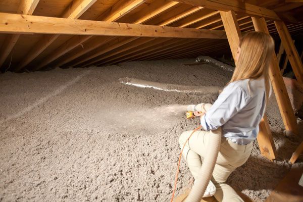 Person in an attic inspecting insulation beneath wooden rafters
