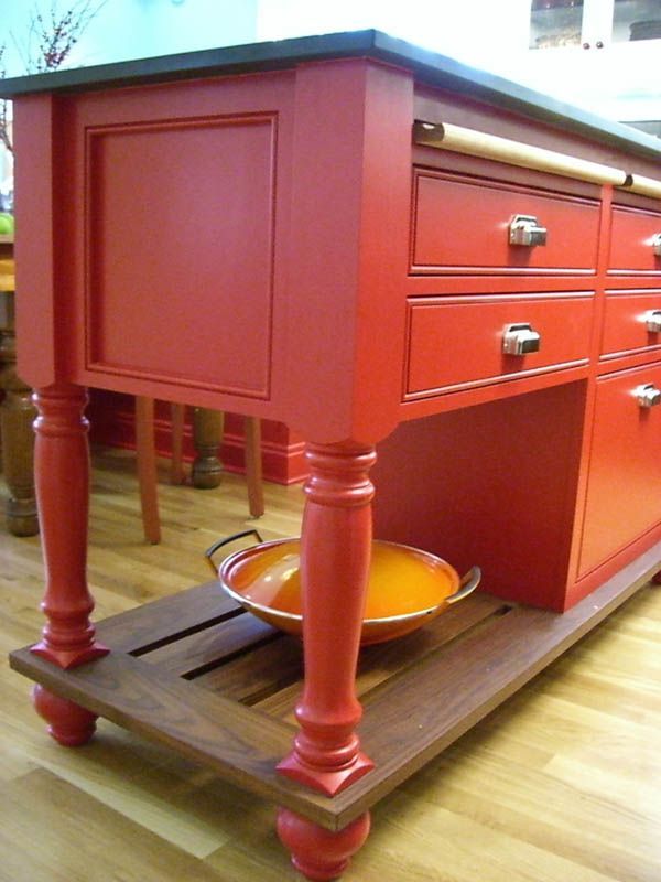 Red kitchen island on casters with drawers and open shelf holding bowls on a wooden floor