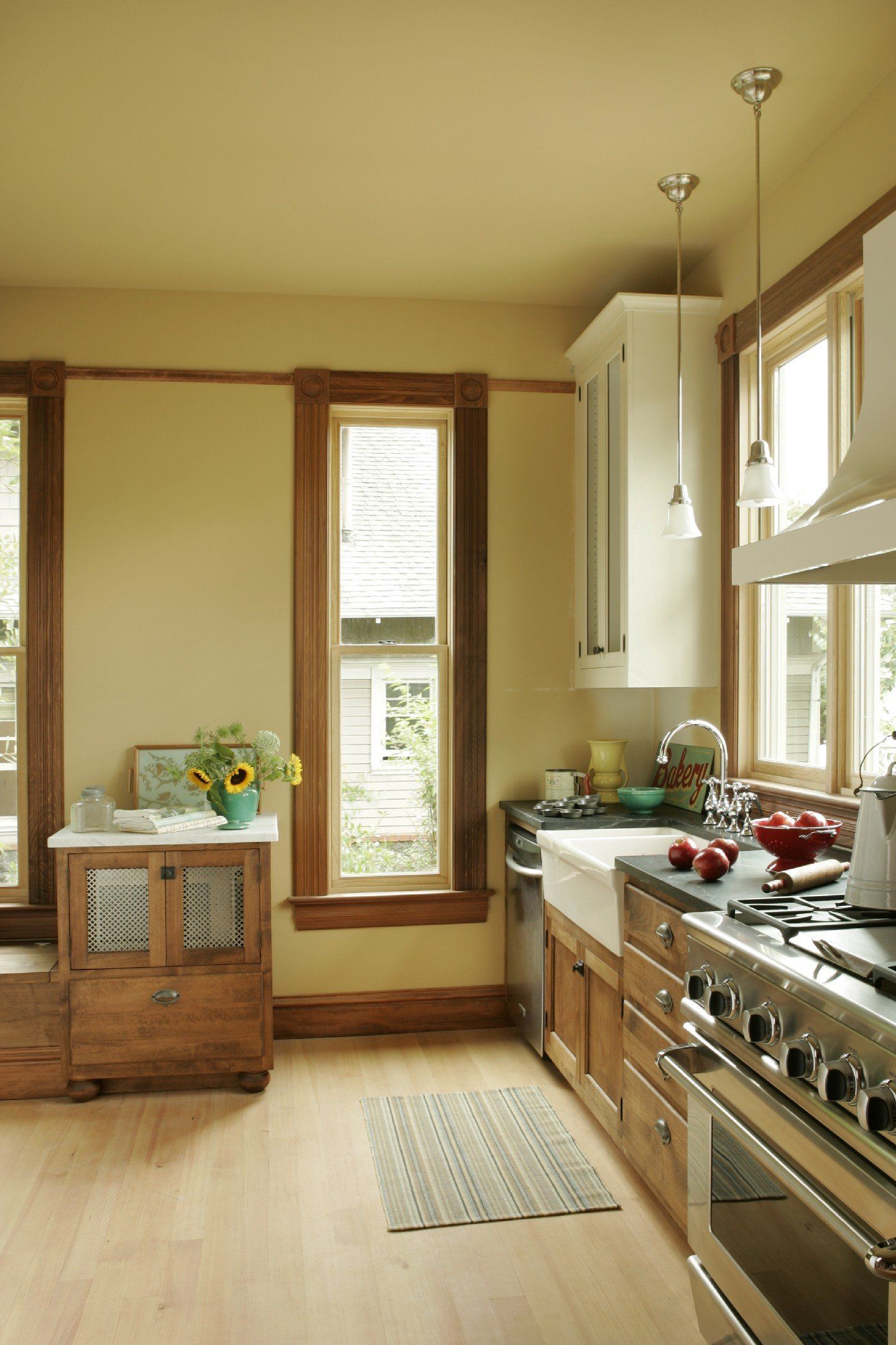 Bright kitchen with wood cabinets, stainless stove, white windows, and a rug on the floor.