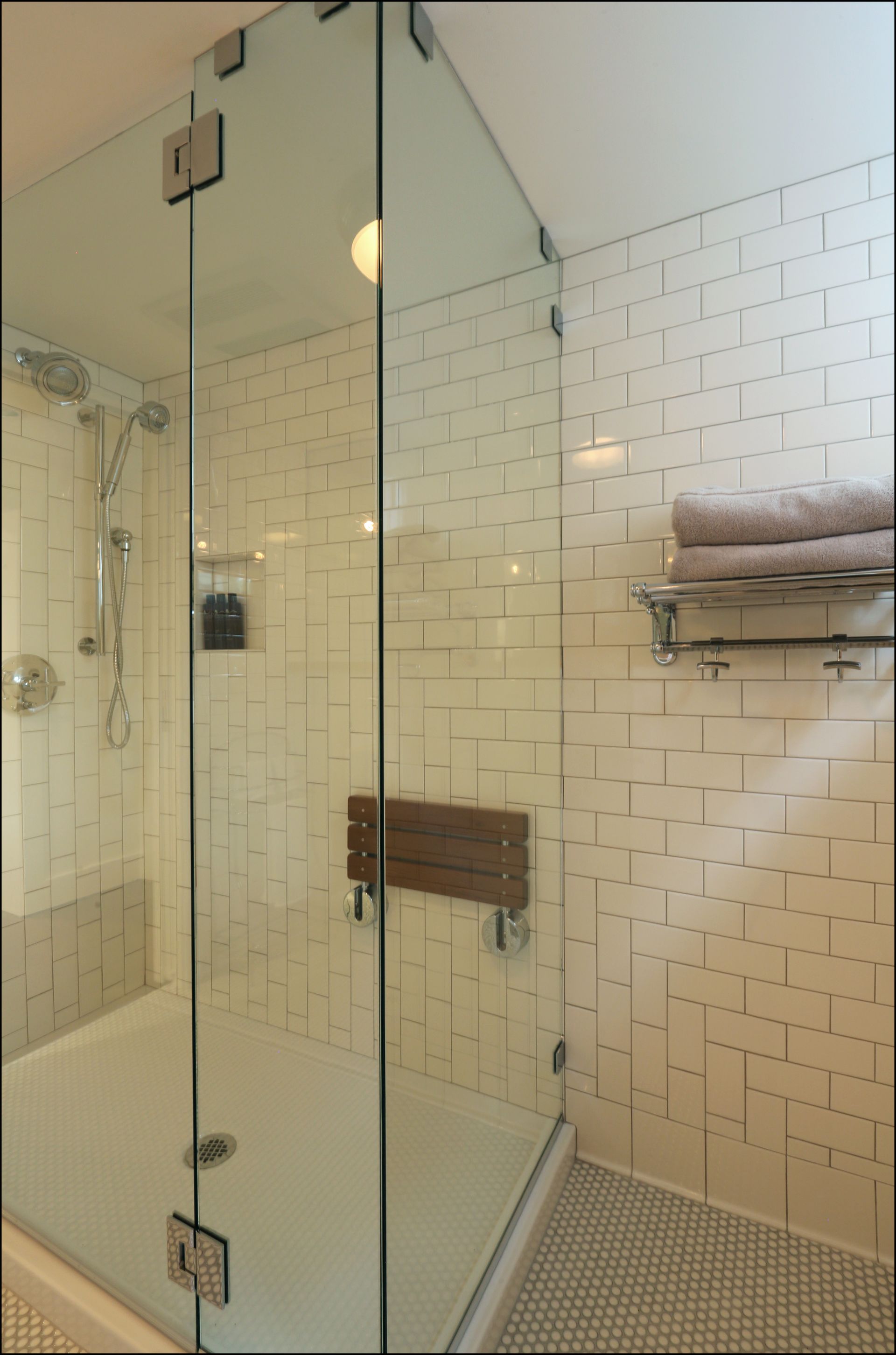 Glass shower stall with white tile walls, built-in shelf, and folded towels on the right