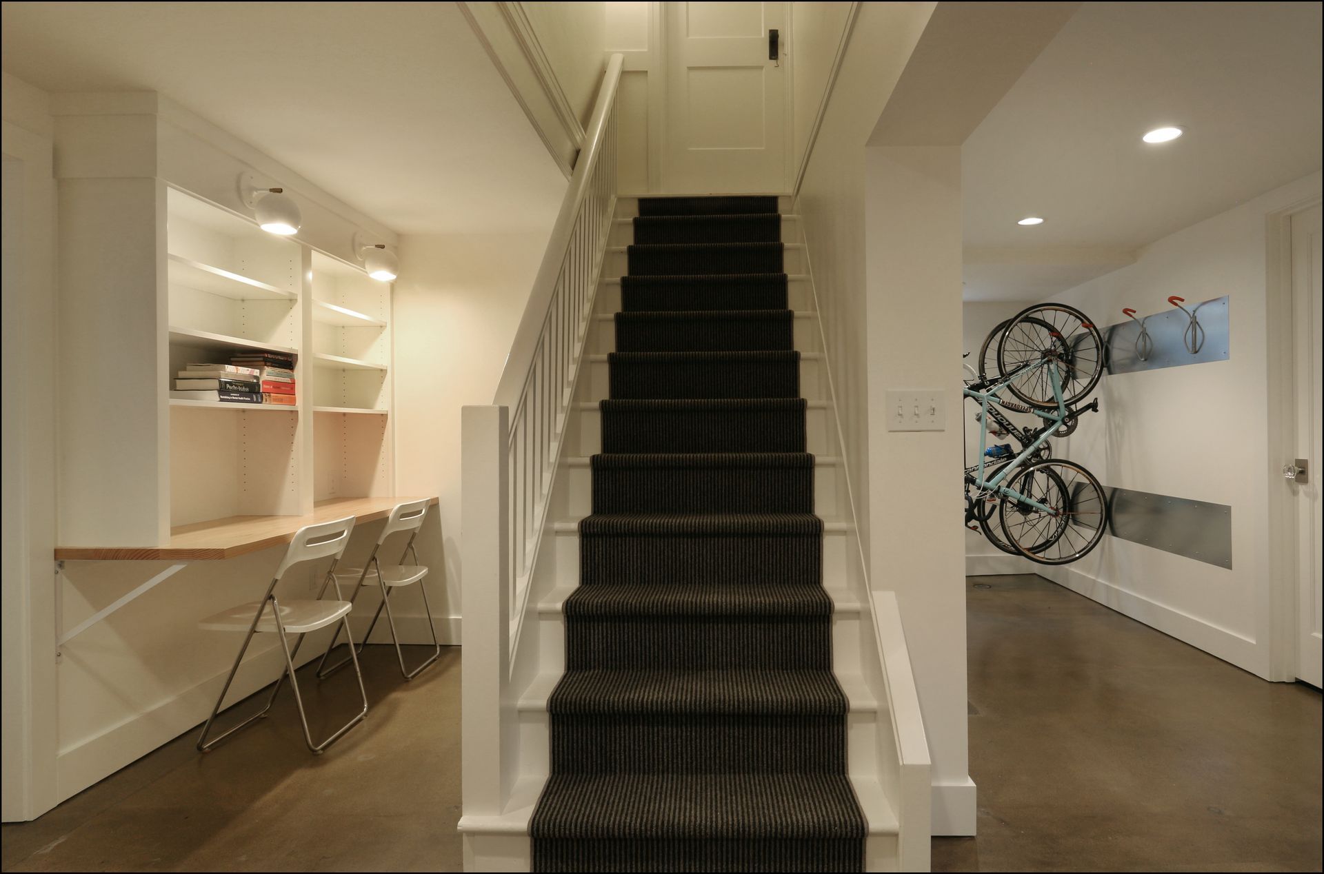 Hallway with a central staircase, a small desk on the left, and wall art in a modern interior.