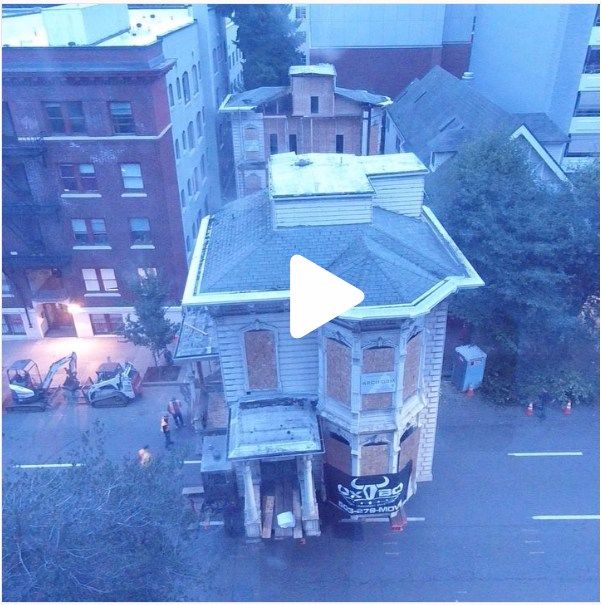 Aerial view of an old brick house on a city street at dusk, with nearby buildings and trees.