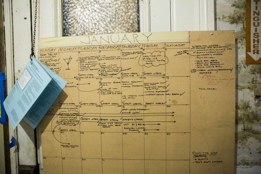 Handwritten January wall calendar on cardboard, with notes and a blue paper pinned at left.