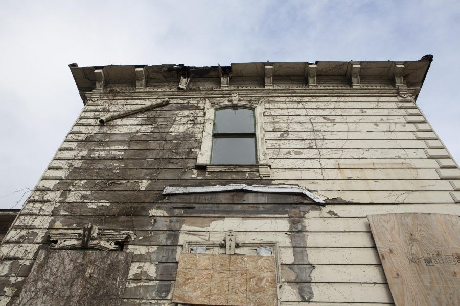Weathered, peeling wooden house facade with a central window and damaged siding.