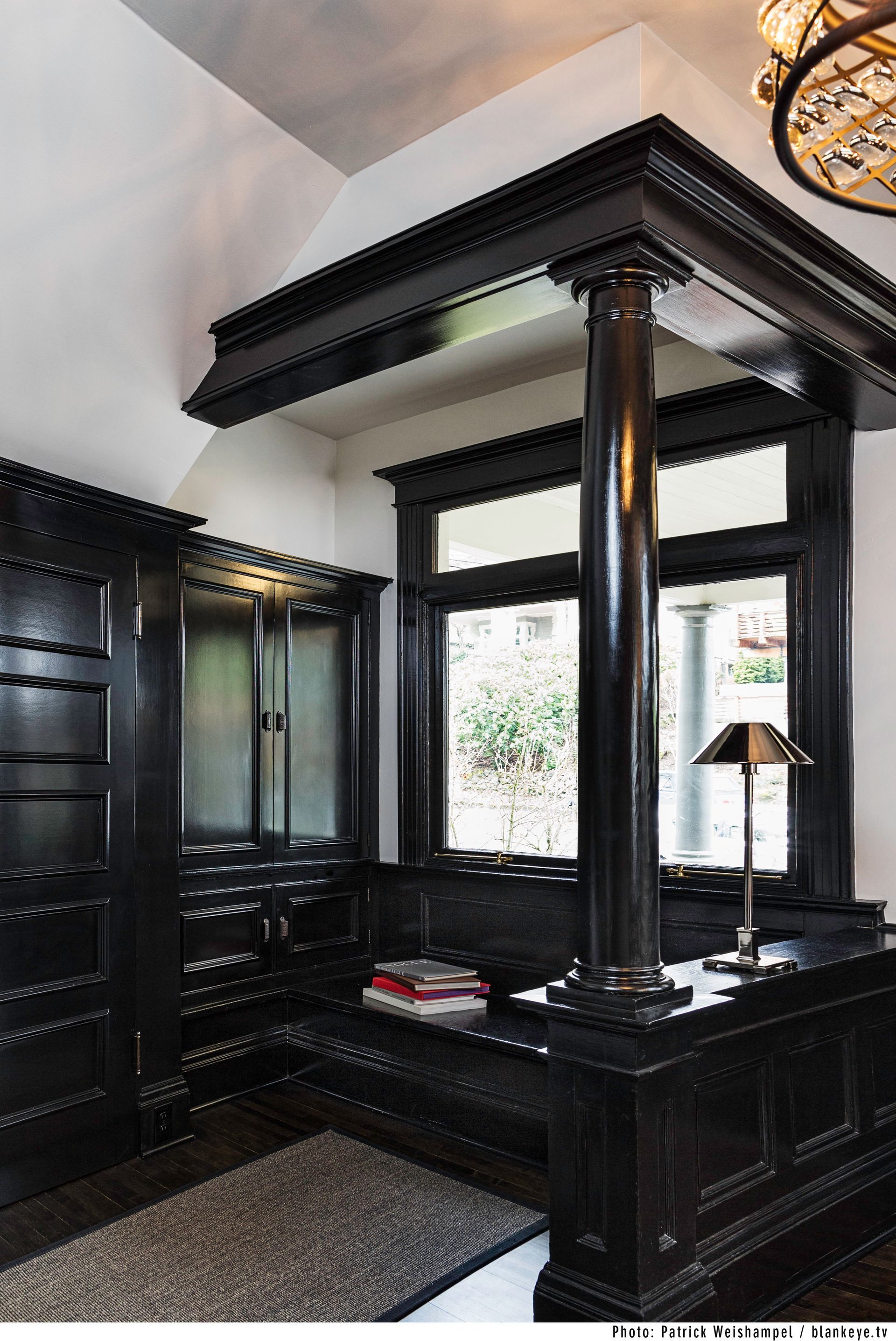 Elegant black four-poster bed in a dark, classic bedroom with a window and lamp.
