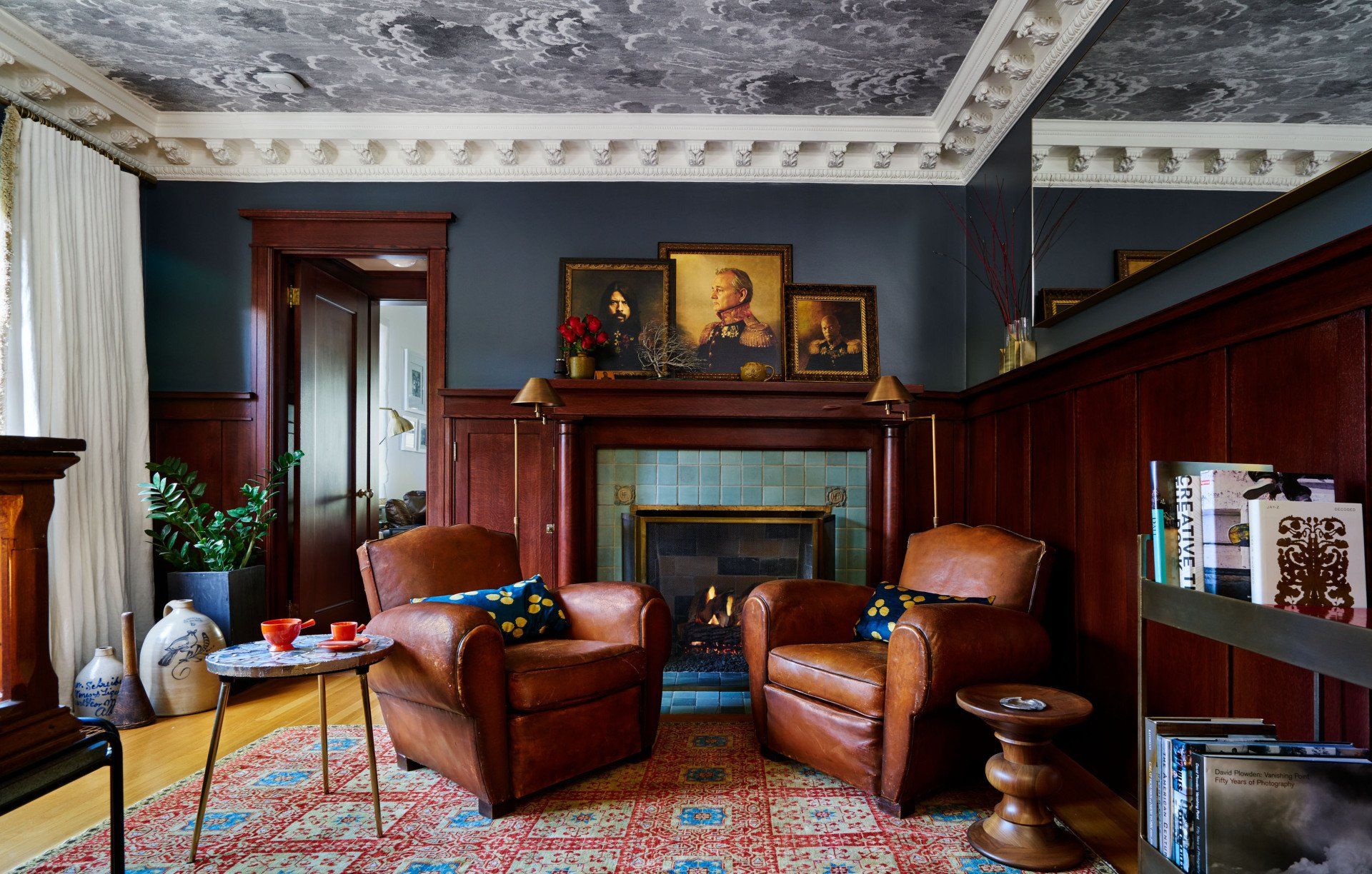 View of the library's fireplace corner, with cozy leather chairs and a peek of the wallpapered ceiling.