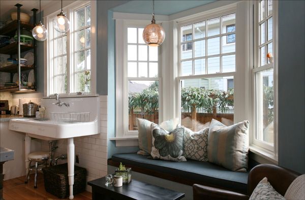 Cozy window nook with cushioned bench, plants, pendant lights, and a white sink in a bright room