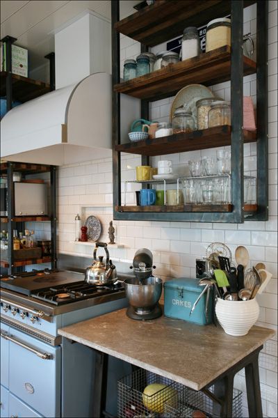 Compact kitchen with stove, white tile backsplash, wooden counter, and open shelves of dishes and jars