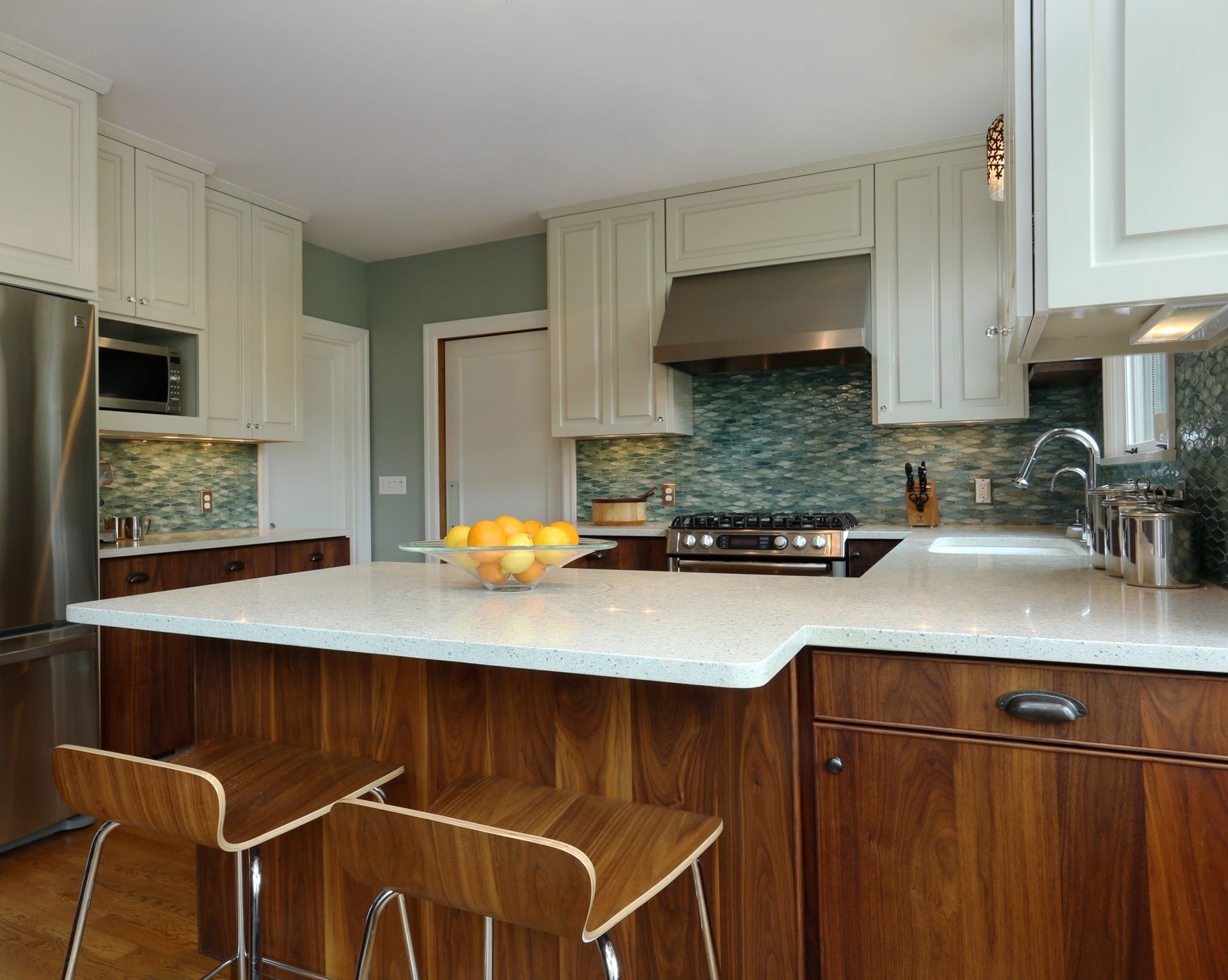 Standing at the walnut island with white ice stone counter, looking at the kitchen's stove wall