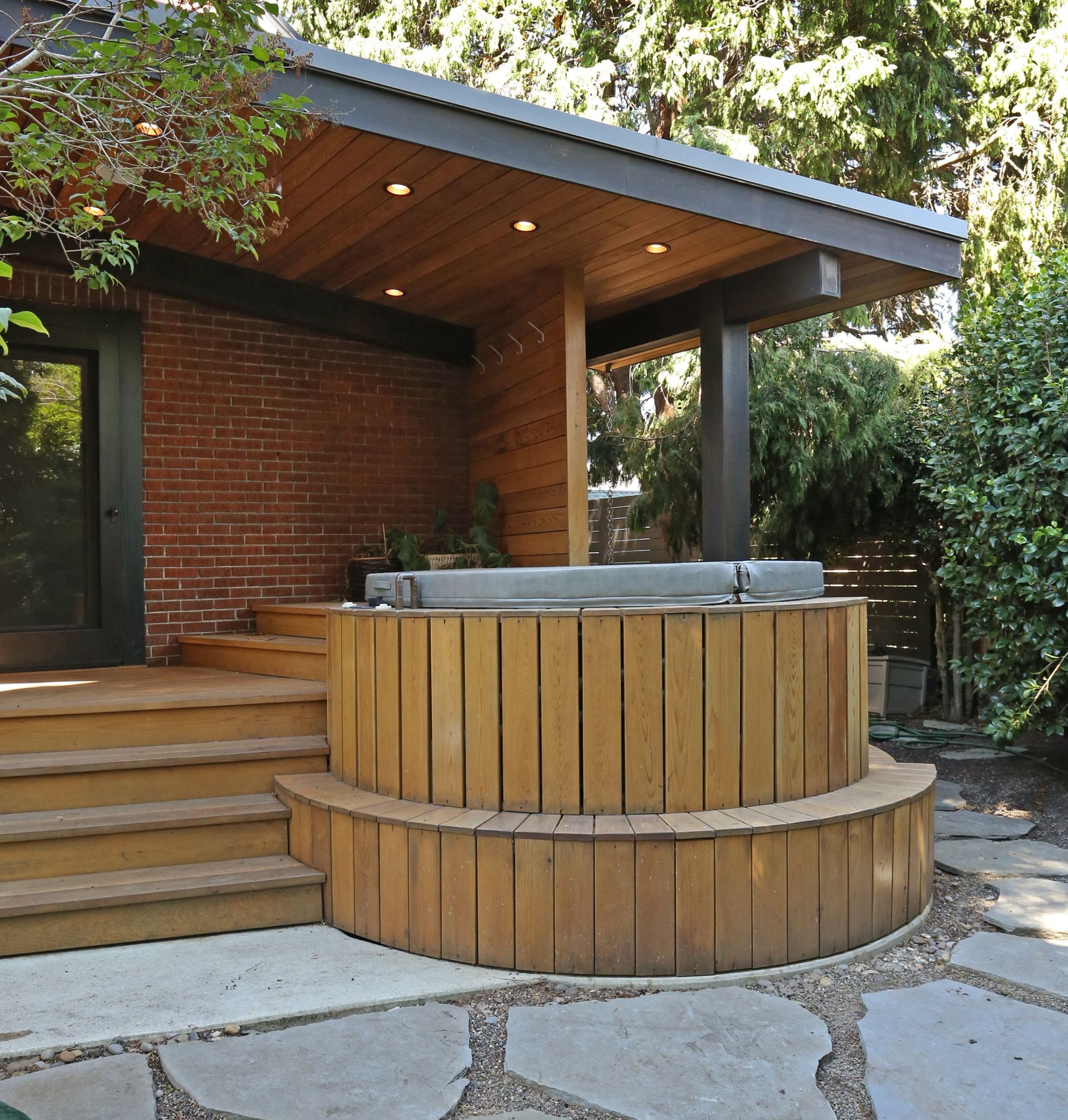 At the back of the brick home, looking at the semi-covered hot tub, deck and stairs