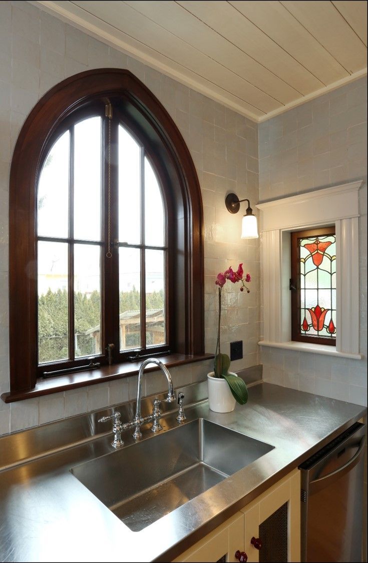 Bright kitchen with arched window, stainless steel sink, and white countertop with flowers and stained-glass accent.