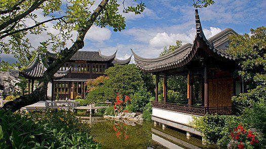 There is a pond in the middle of a garden with a building in the background.