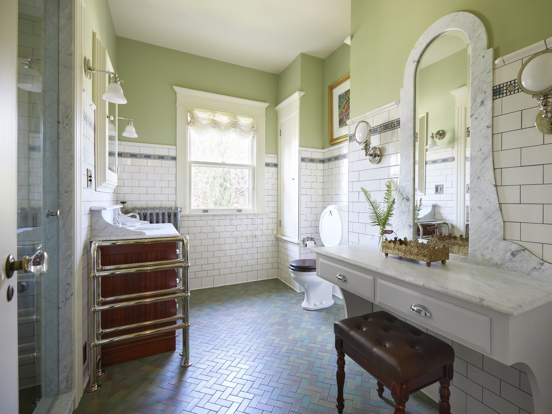 In the remodeled guest bath,  the original pillbox toilet was restored. A makeup counter with marble top and mirror frame, floor mounted towel warmer, steam shower and new tile to match the old make this room feel like it was always there. 