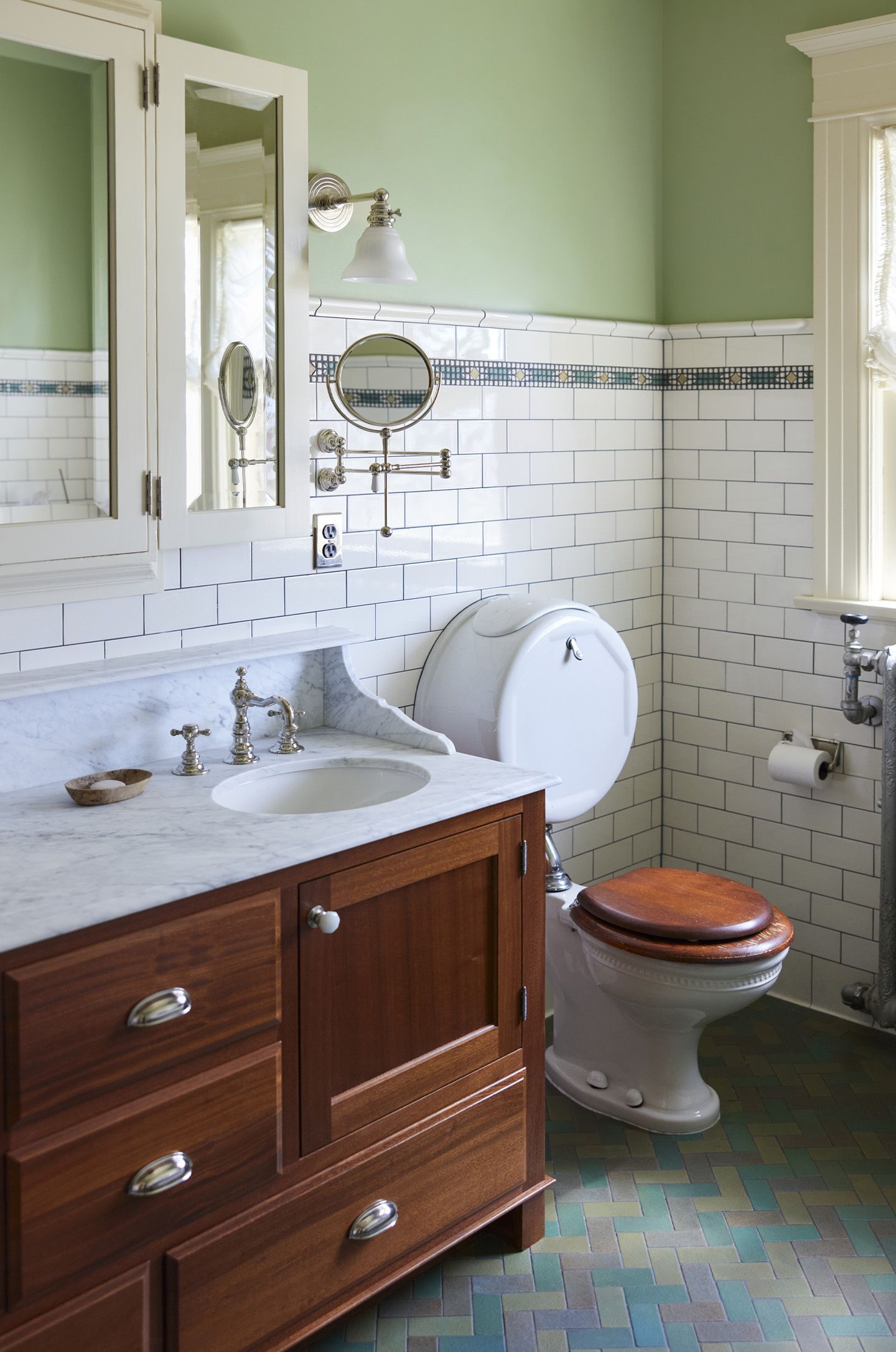 Closer view of the mahogany vanity with two sinks and the restored pillbox toilet near the original radiator. 
