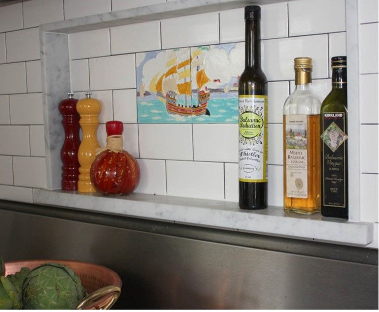 Kitchen counter with colorful condiment bottles, a wine bottle, and a painting of a sailing ship on tiled wall.