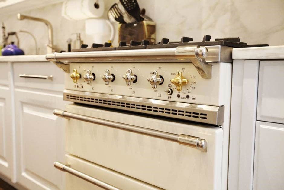 Cream-colored vintage stove in a bright kitchen with brass knobs and a metal handle