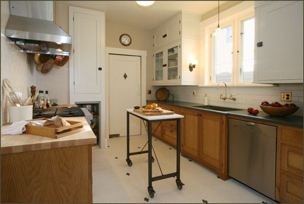 Bright kitchen with white cabinets, wooden counters, and a rolling worktable in the center.