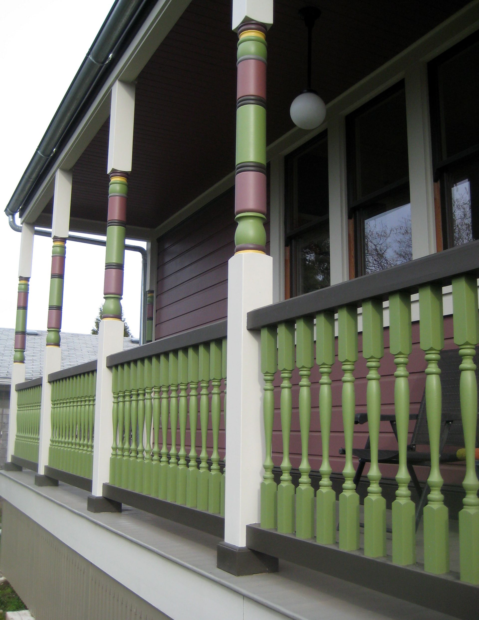 Colorful Victorian porch with green railing, pink columns, and white trim on a house exterior.