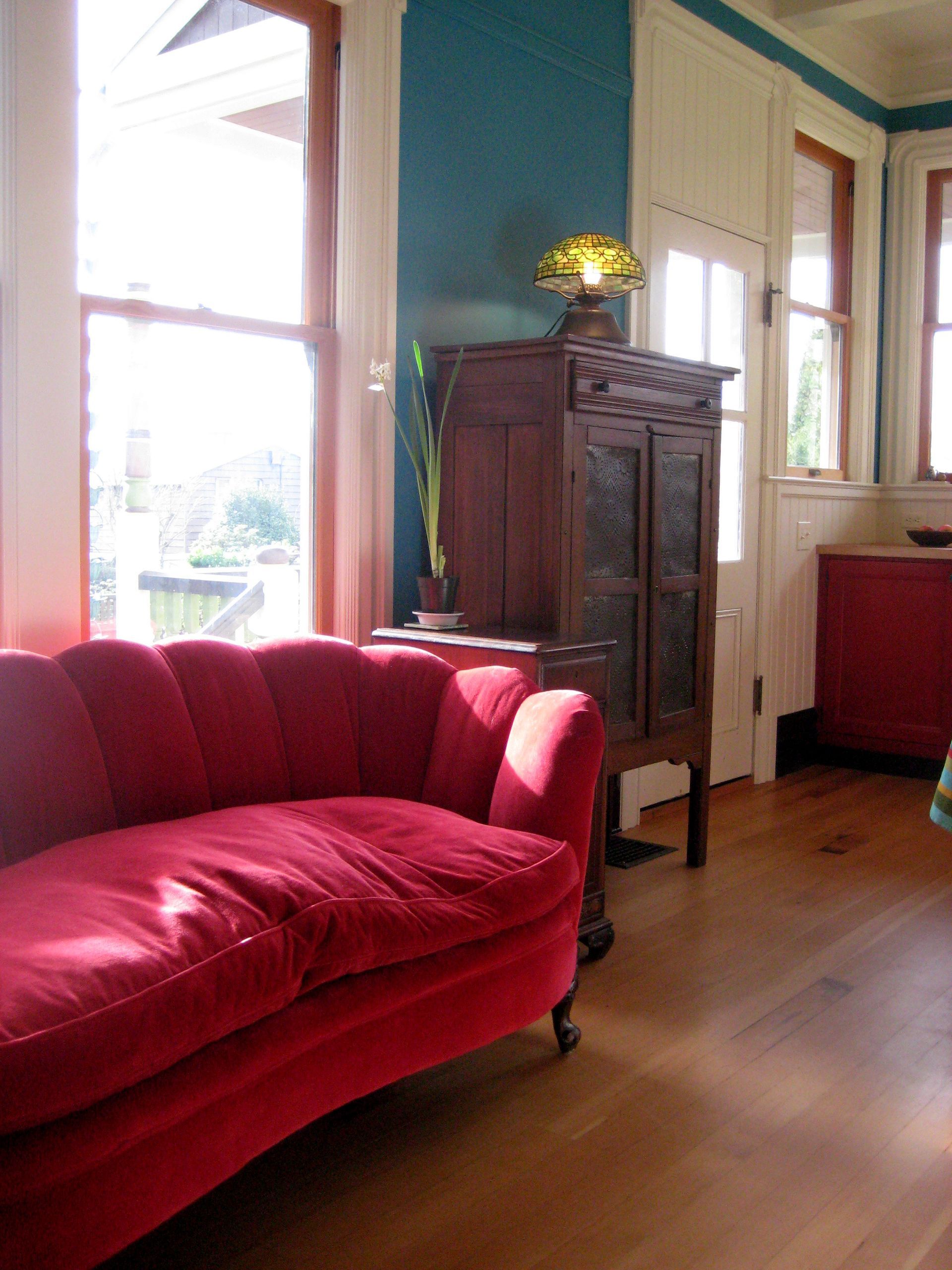 Red chaise lounge in a bright living room with wooden floors and a dark cabinet by the window
