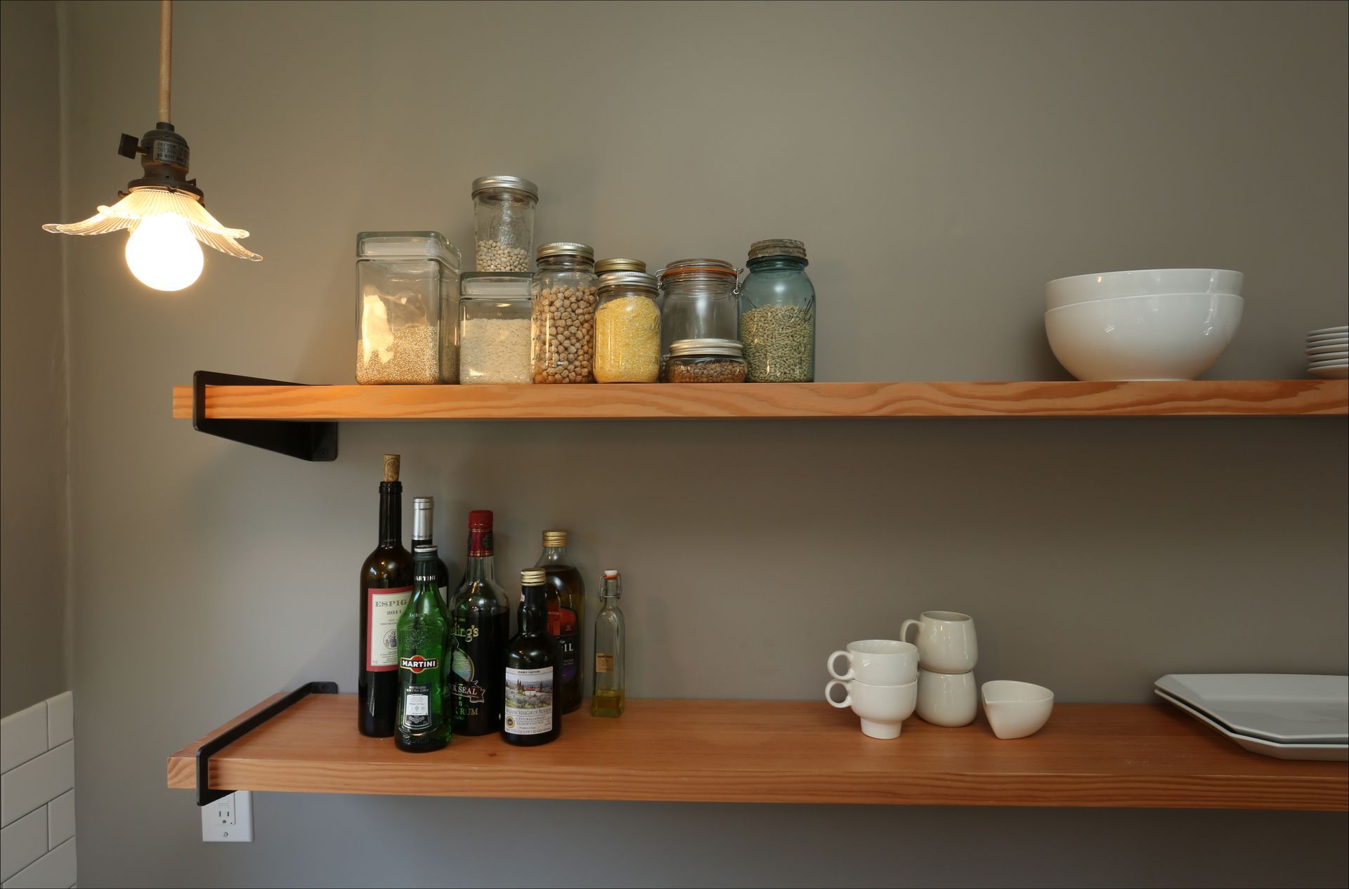 Wooden shelves with glass jars, bottles, cups, and plates in a small kitchen nook