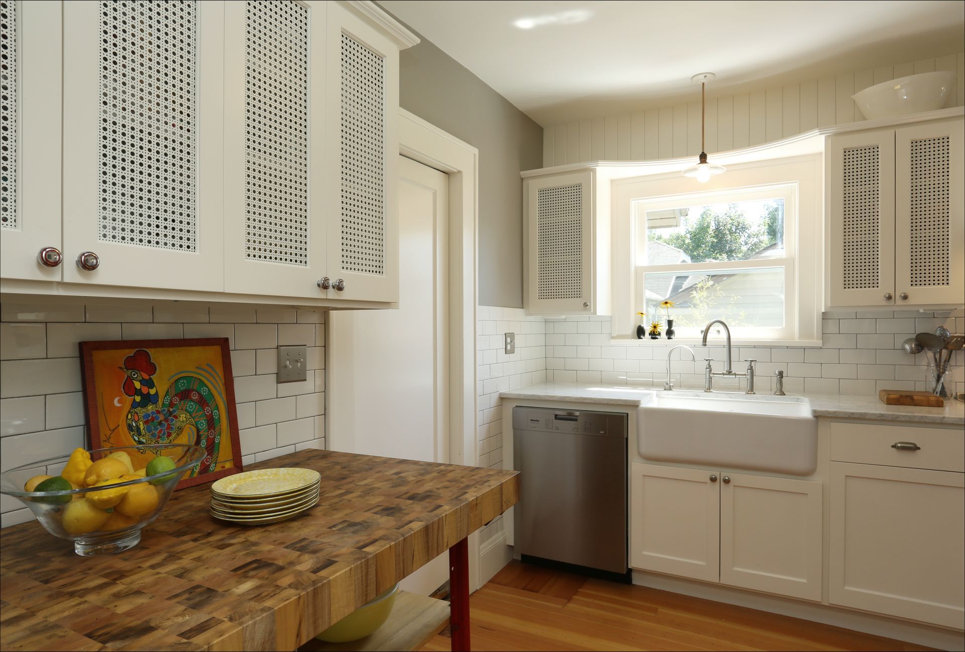 Bright kitchen with white cabinets, wood table, sink by window, and fruit on the counter