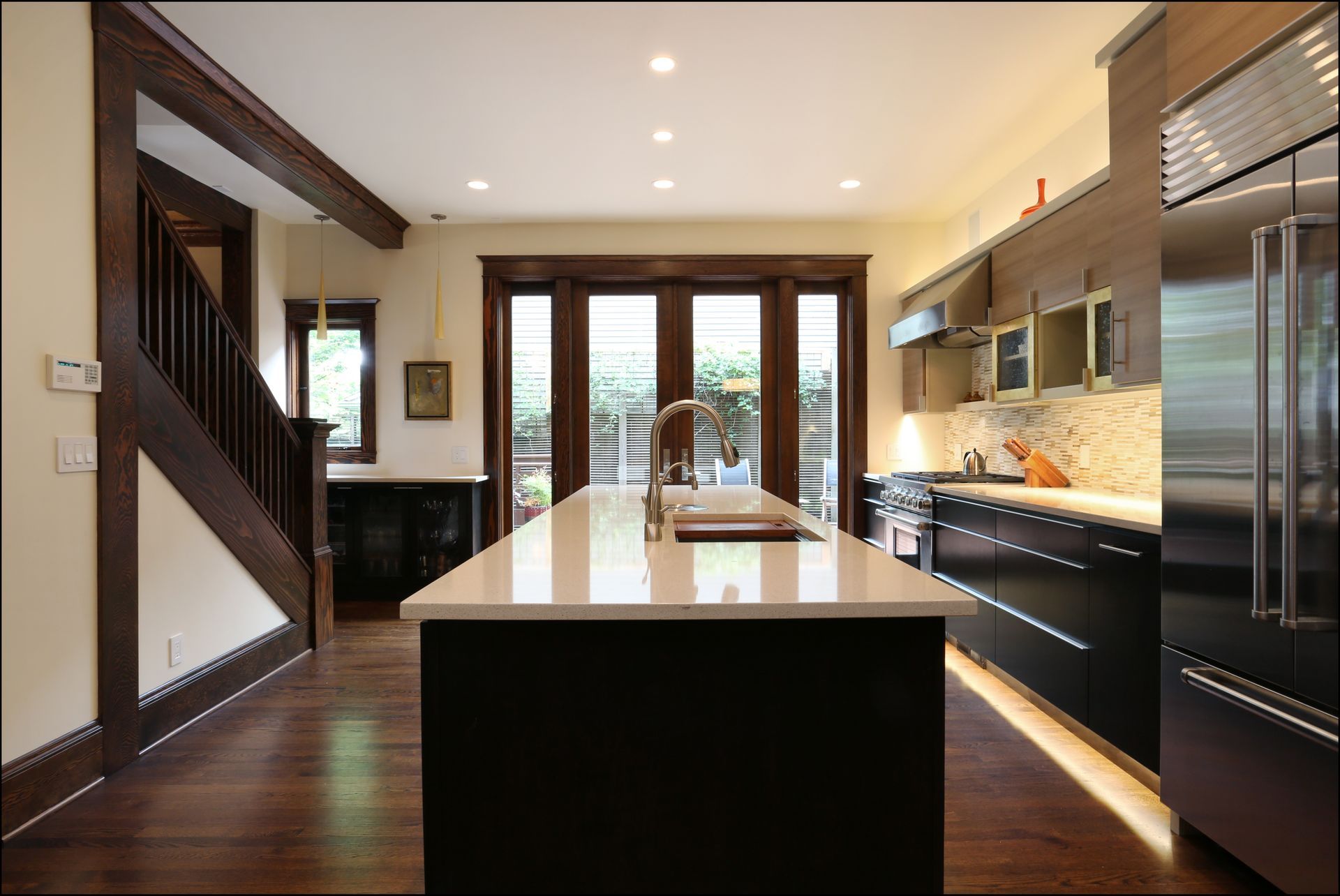 Modern kitchen with a large island, dark cabinets, stainless steel appliances, and hardwood floors