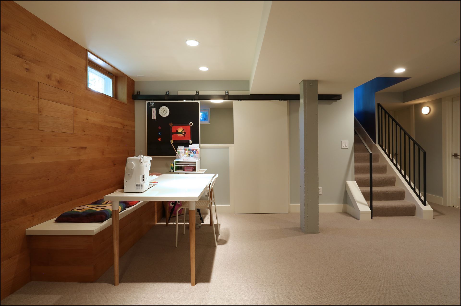 Basement rec room with work table, wood-paneled wall, and staircase to upper floor