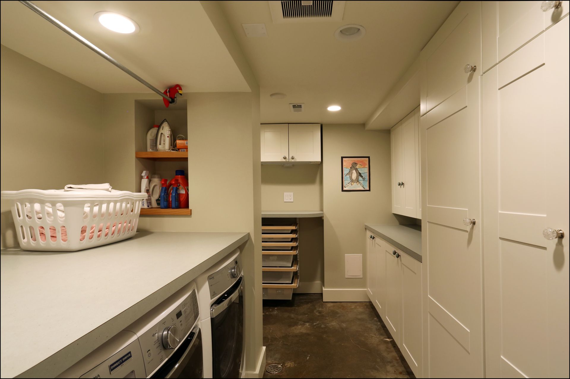 Bright laundry room with white cabinets, counter, washer and dryer, and a small staircase in back.