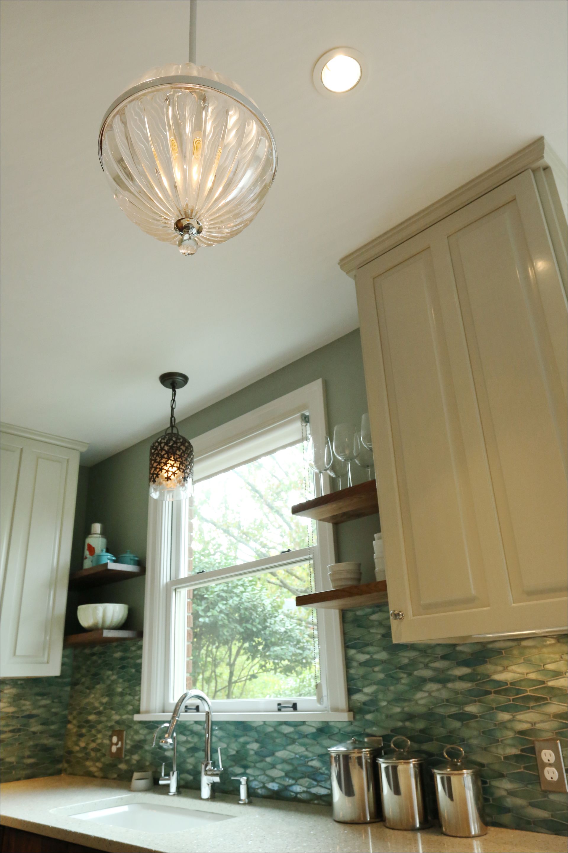 Bright kitchen with cream cabinets, green mosaic backsplash, window, pendant lights, and countertop canisters