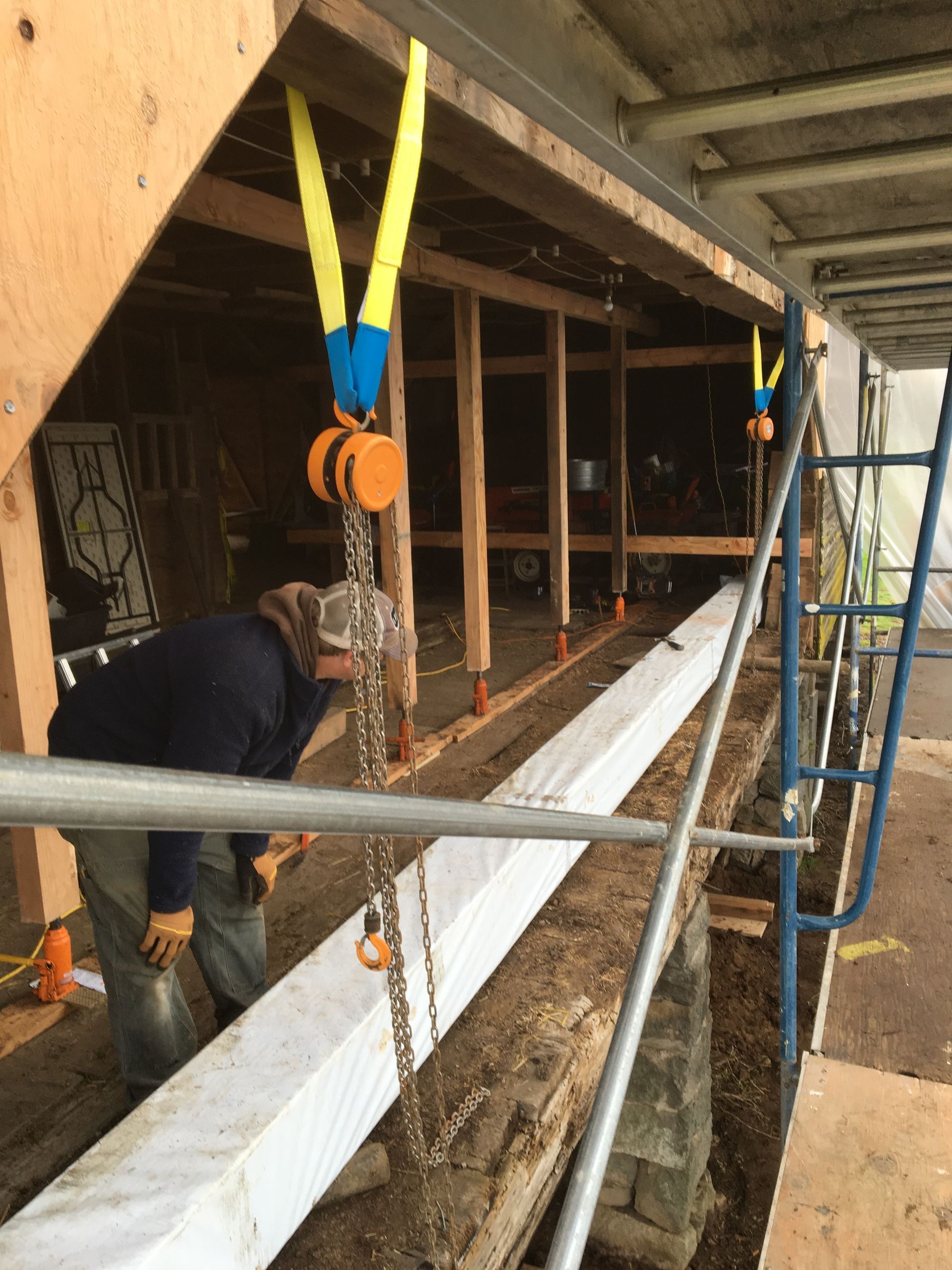 Workers installing a long white beam in a wooden construction frame, with lifting straps and a ladder nearby