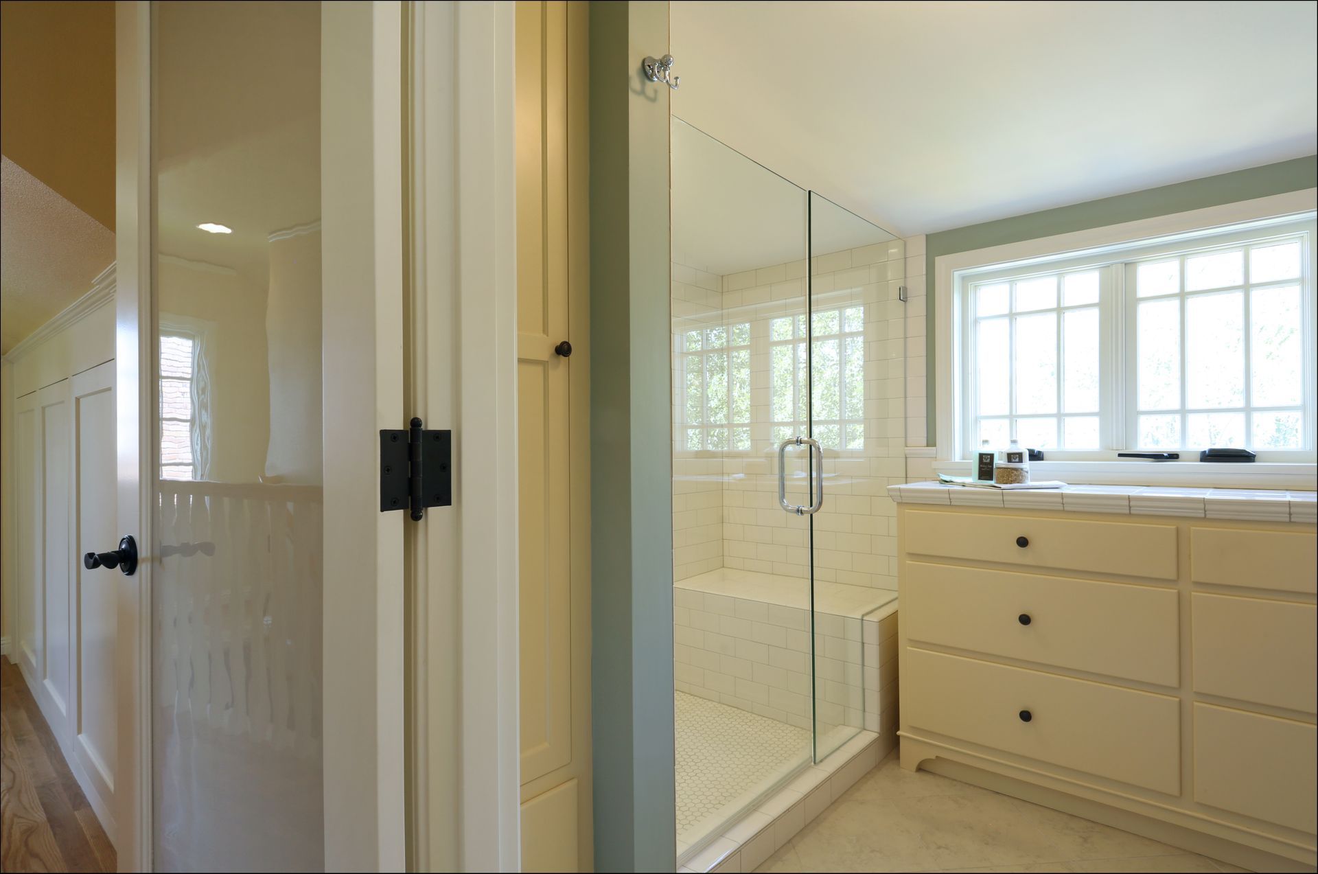 Bright bathroom with glass shower, cream vanity, and large window with blinds