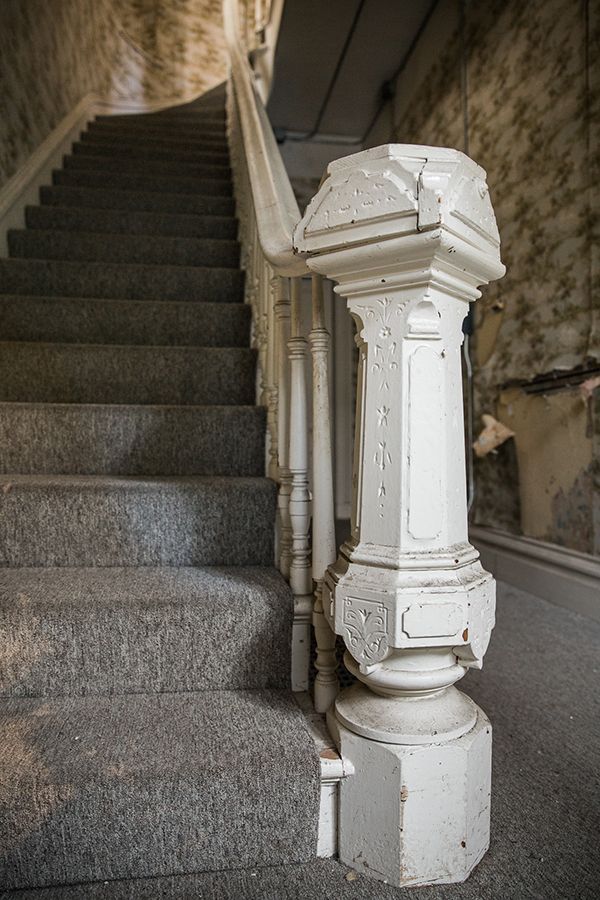 Old staircase with ornate white banister in a dim, narrow hallway