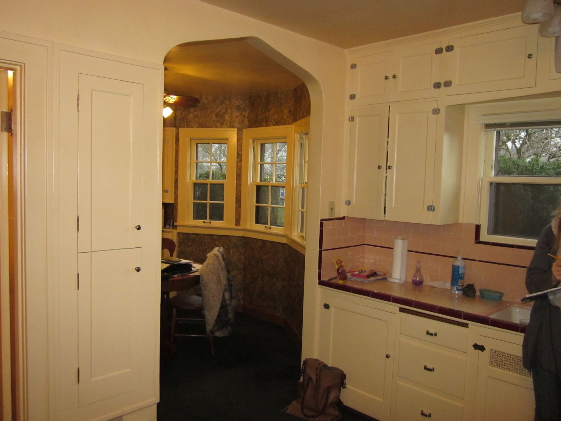 Small kitchen with white cabinets, beige tile backsplash, and an arched doorway to a dining nook.