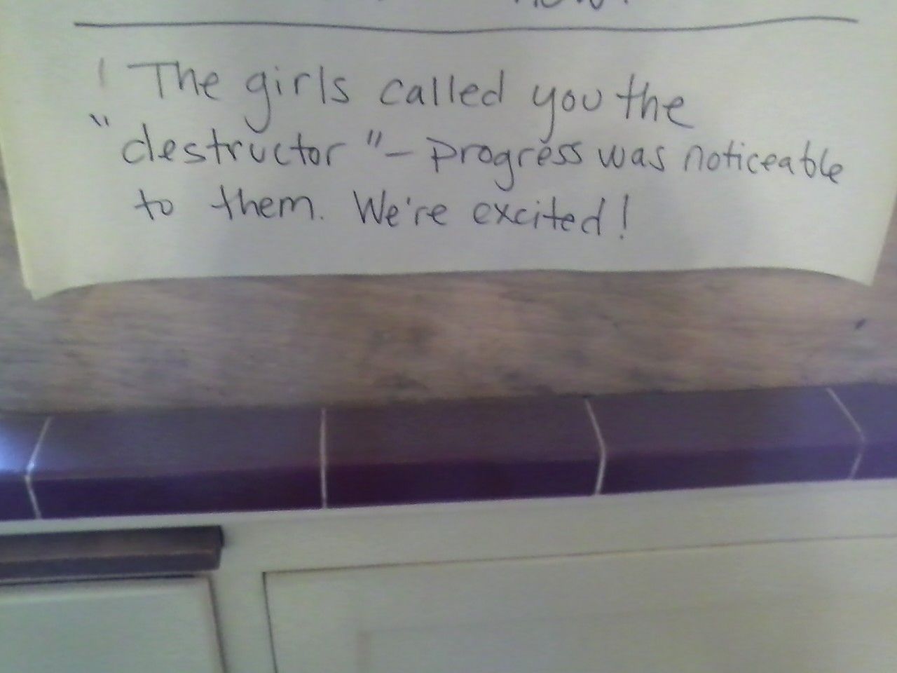 Handwritten note on white paper taped above a doorway, with a quote about “the girls” and progress.