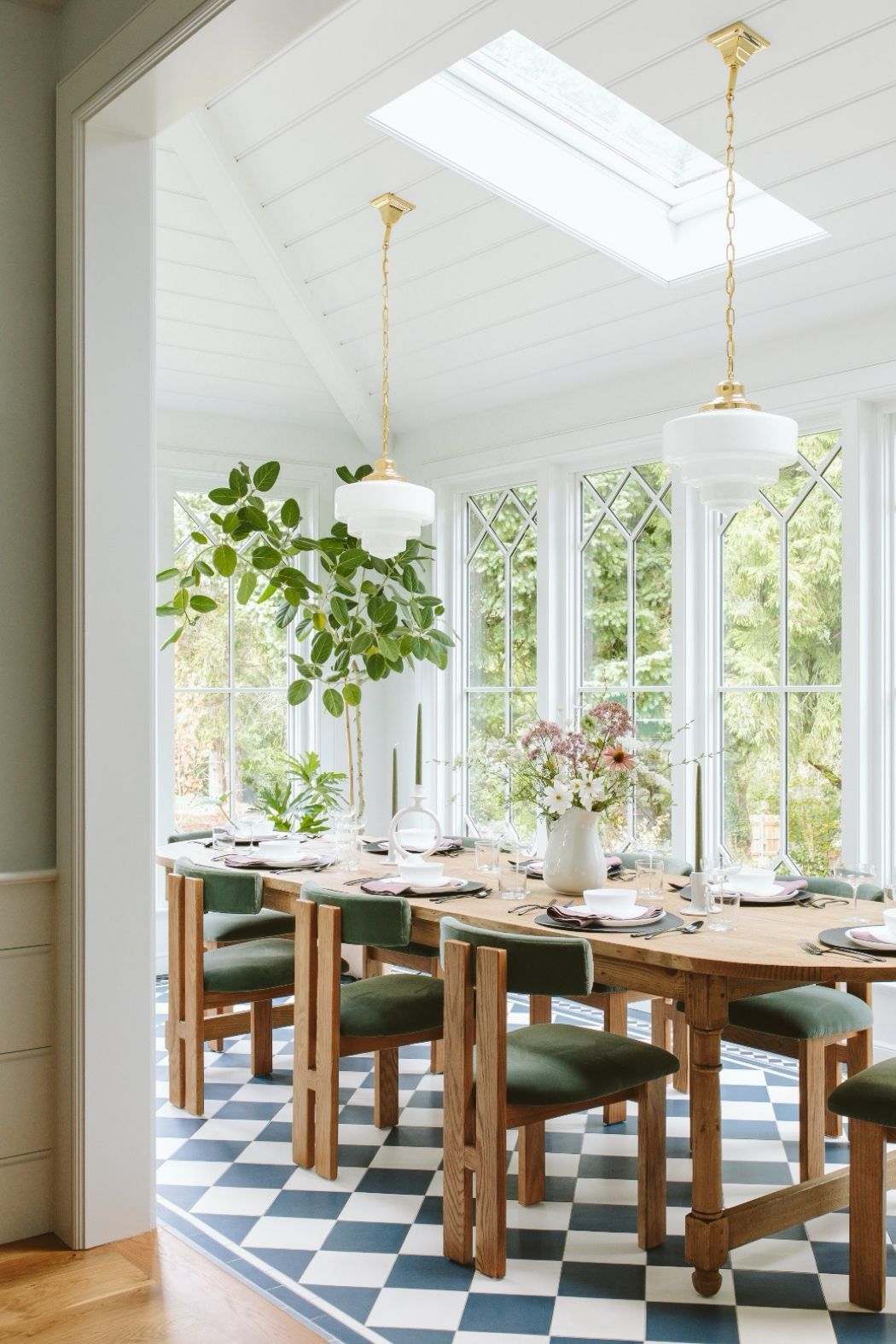 Dining room with checkered floor, long wooden table, green chairs, and large windows.