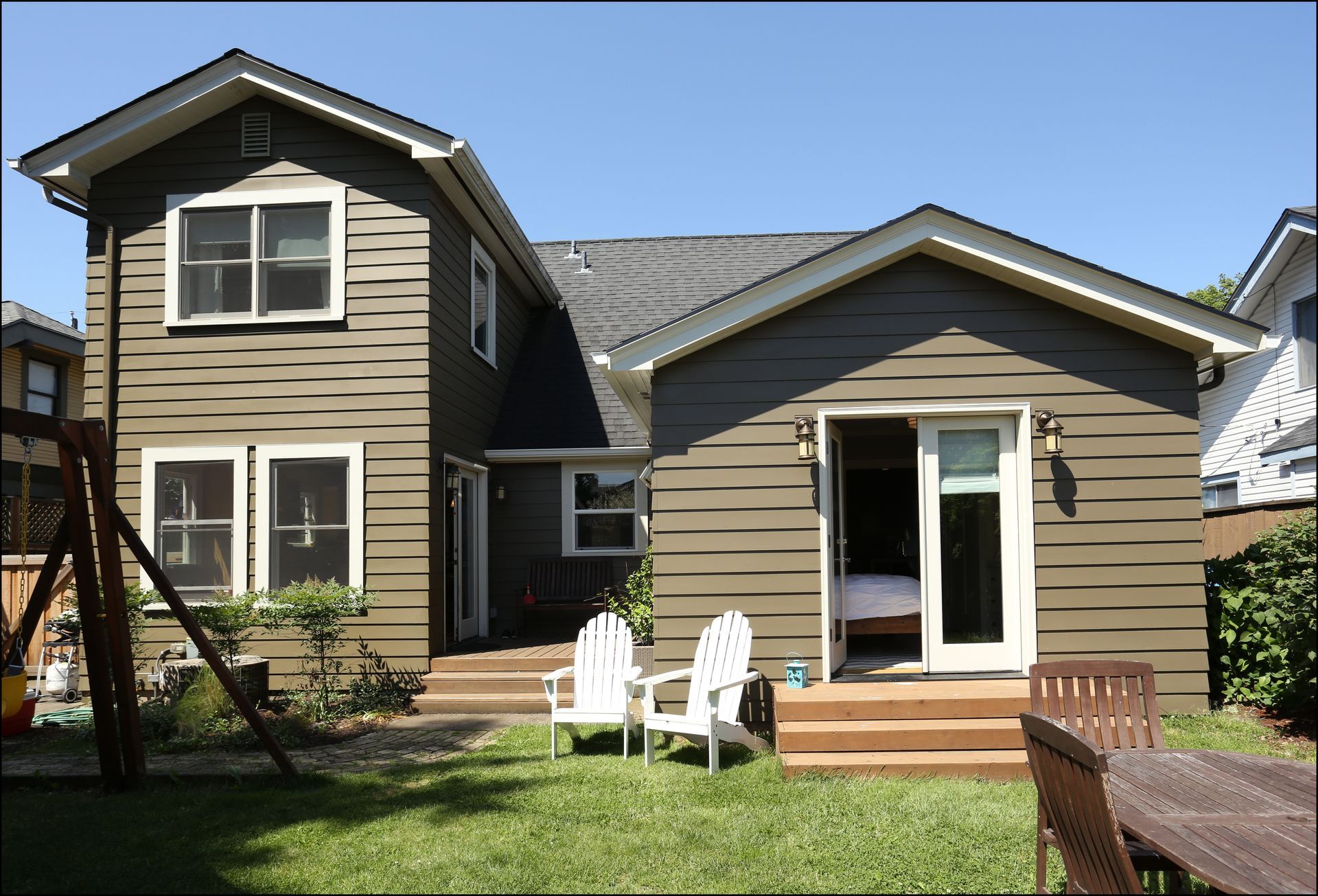 Backyard view of a tan house with white patio chairs, sliding door, and green lawn