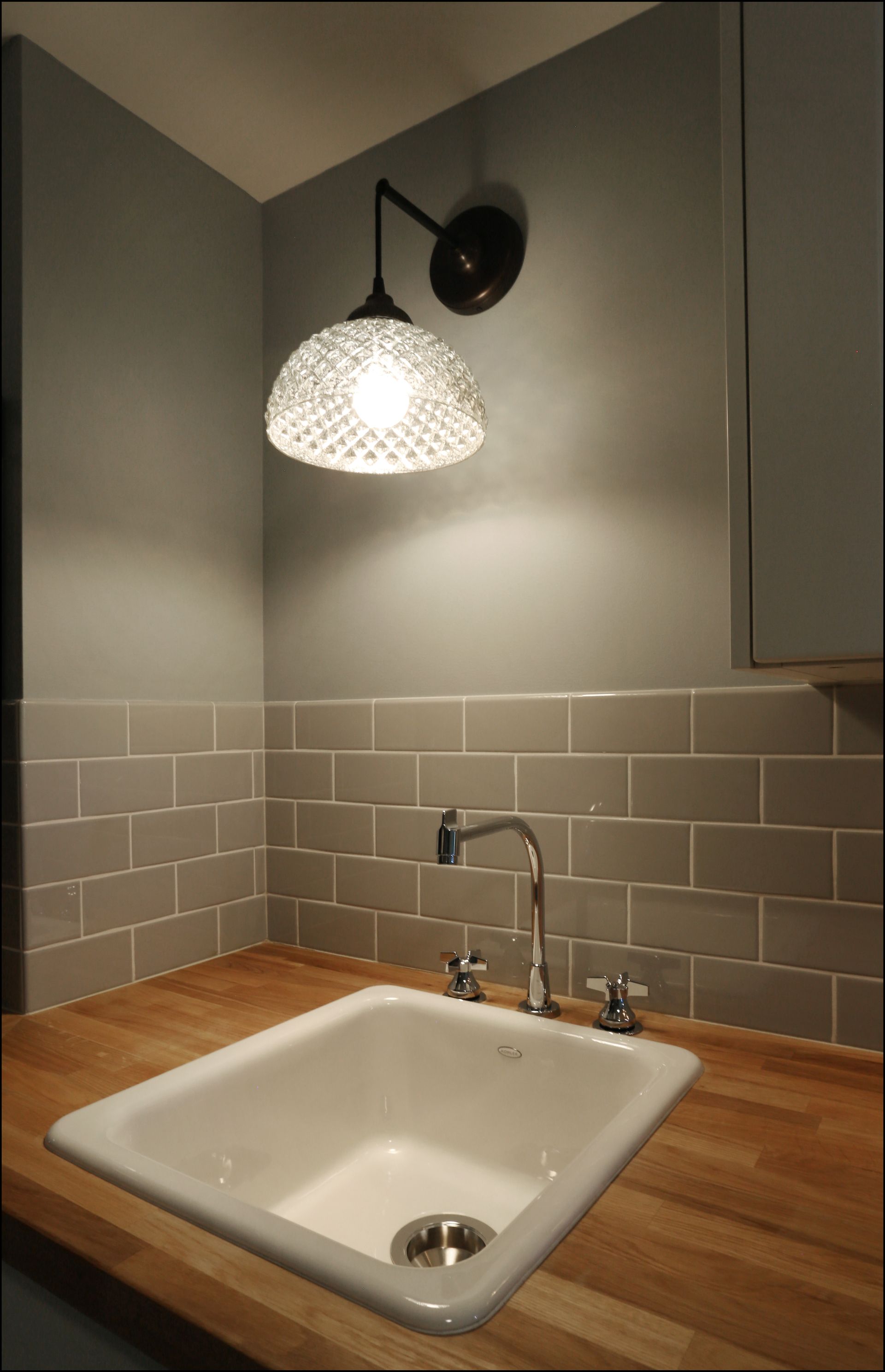Modern kitchen sink with wooden countertop, gray tile backsplash, and hanging patterned wall lamp