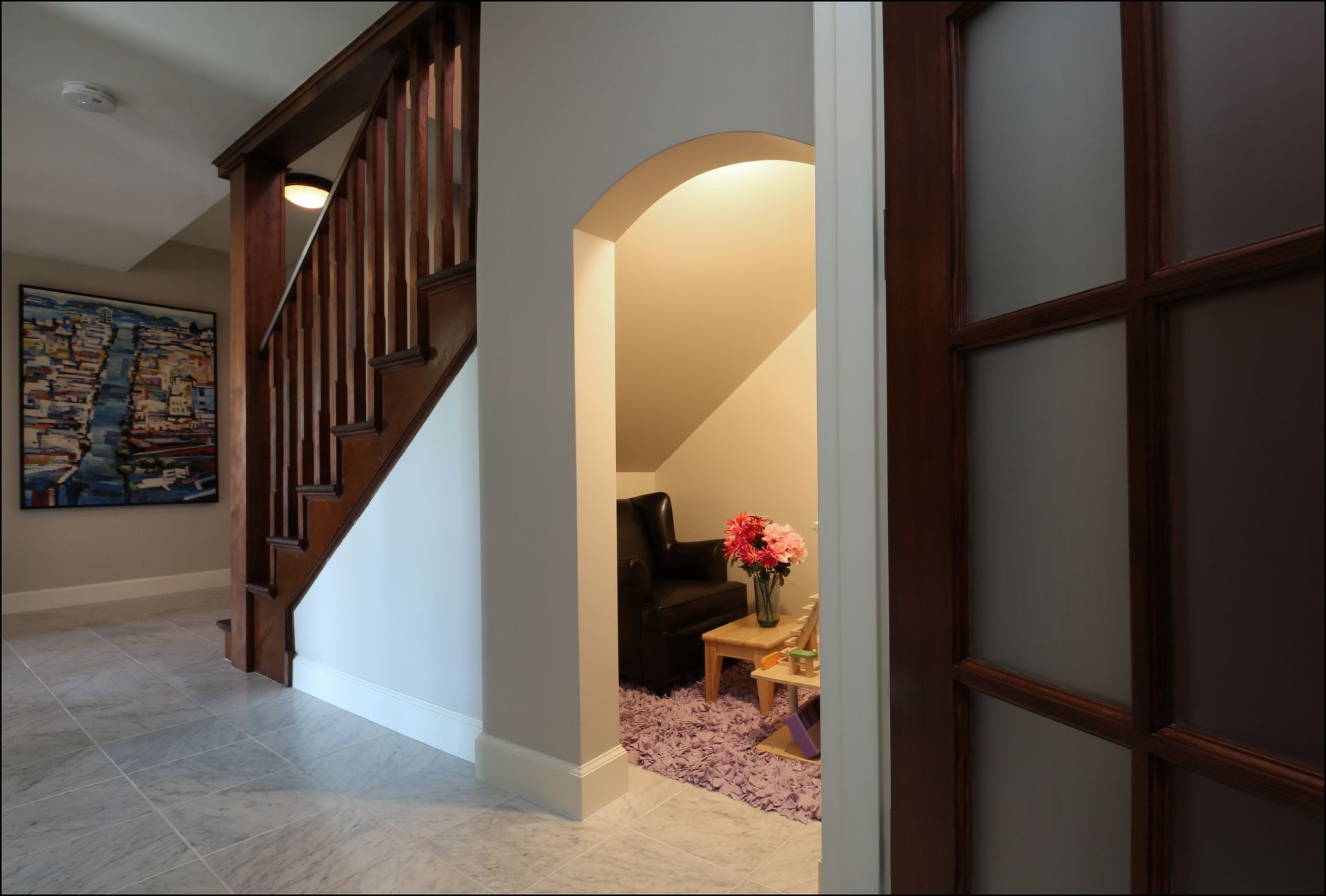 Hallway with carpeted stairs, arched nook with flowers, and dark wood-framed glass doors