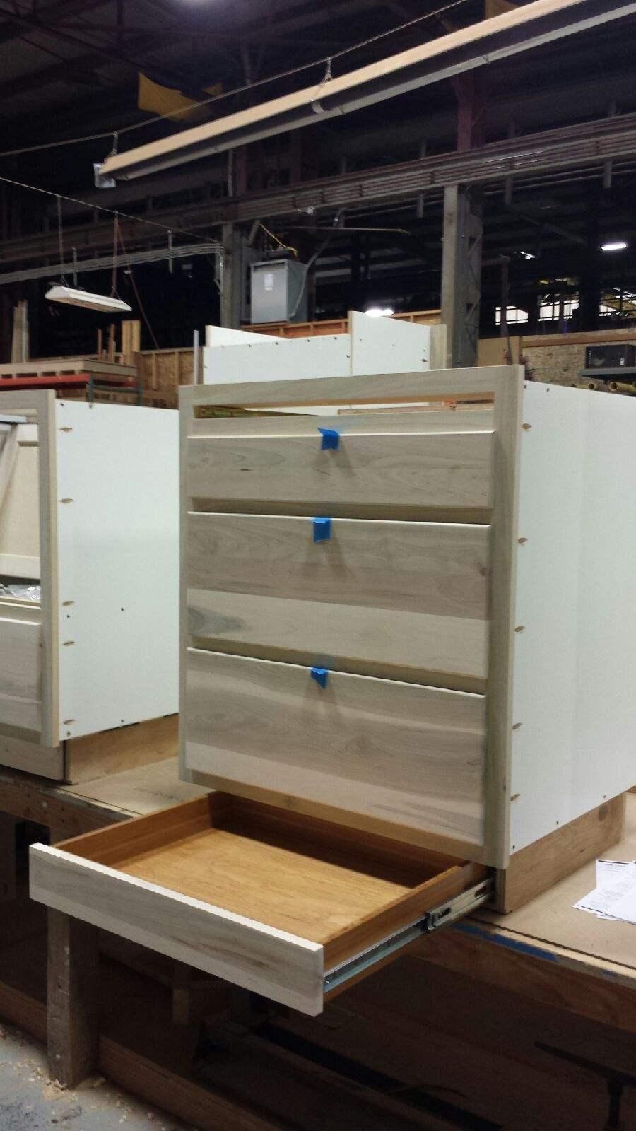 Open drawer cabinet with beige drawers and blue pulls in a warehouse setting