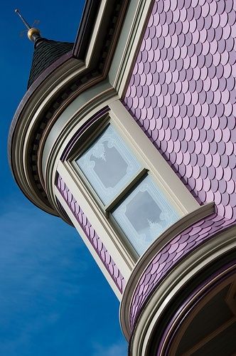 Tilted view of a purple Victorian turret with a white-framed window against a blue sky