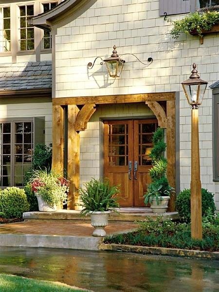Cozy house entrance with wooden doors, stone facade, lanterns, and potted plants by a wet path