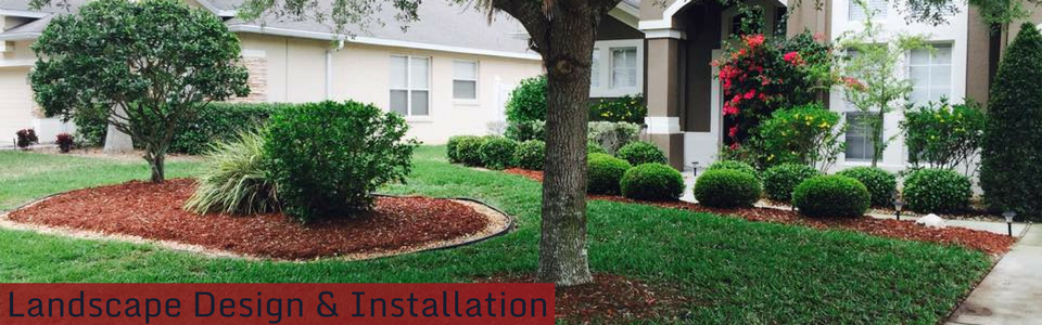 Landscaped front yard with shrubs, trees, and red mulch beside a house, labeled “Landscape Design & Installation”
