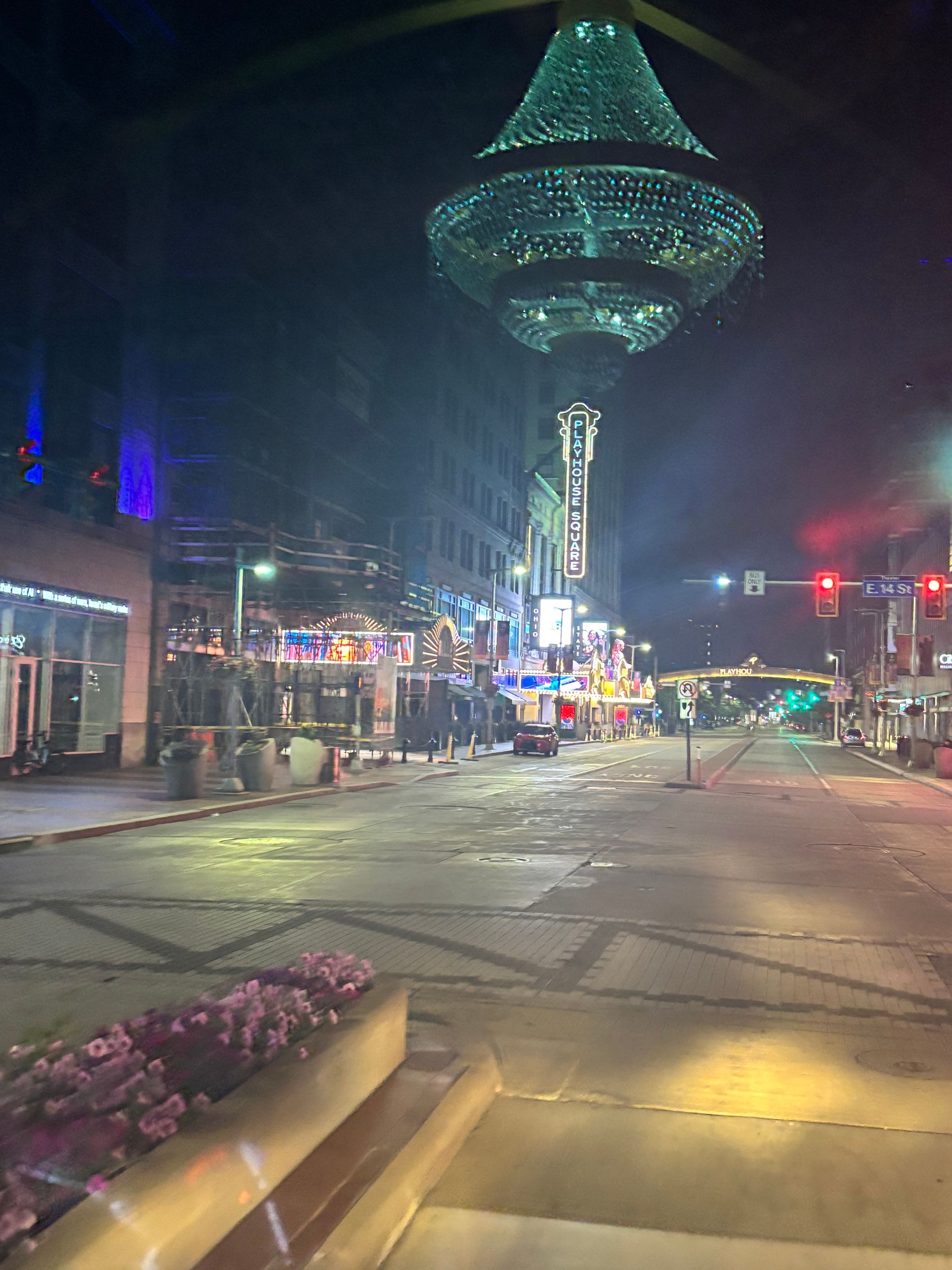 Nighttime city street with a large illuminated chandelier sculpture and festive lights near a crosswalk