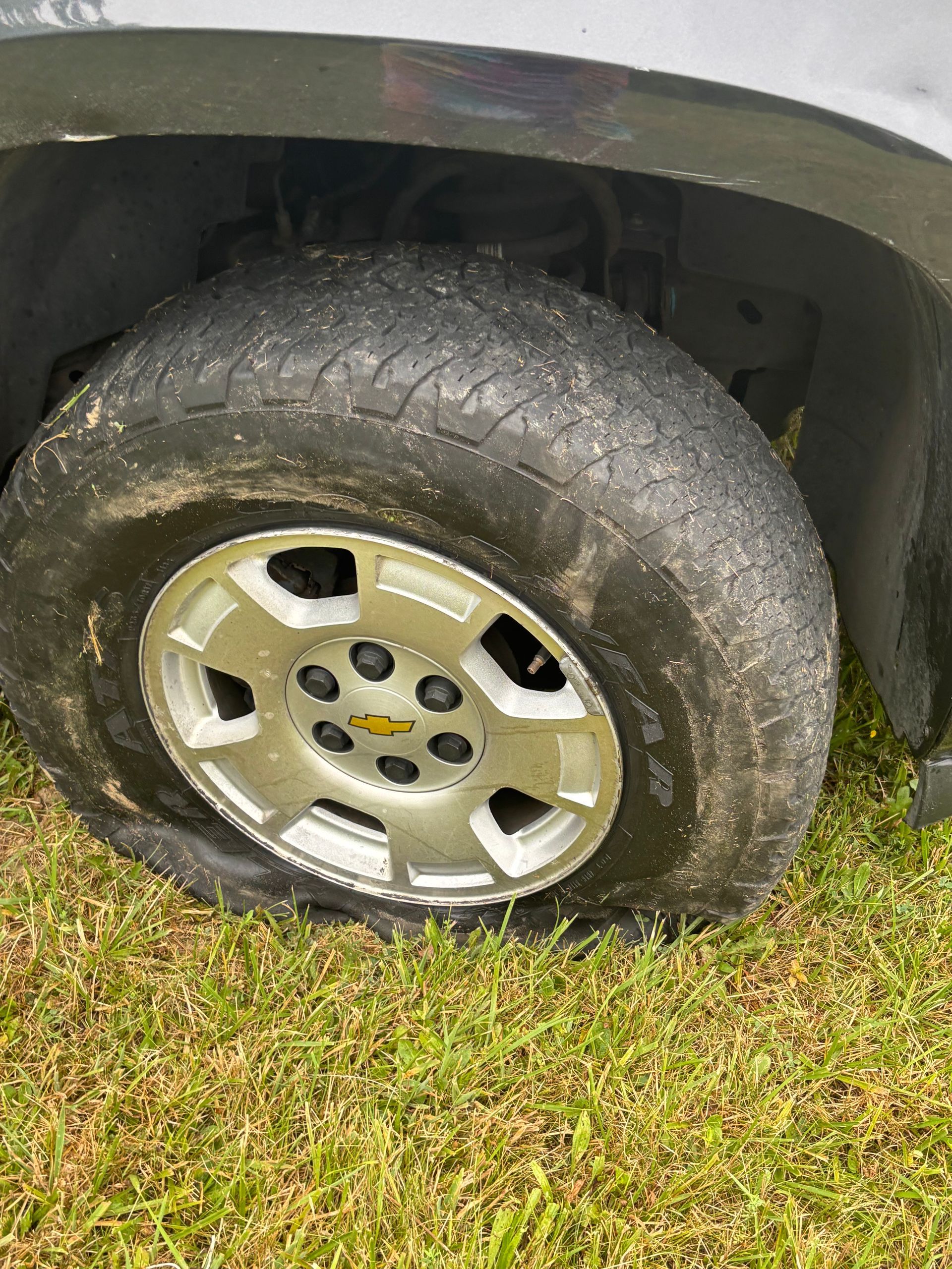 Close-up of a dirty car tire and silver wheel on grass beneath a black vehicle fender