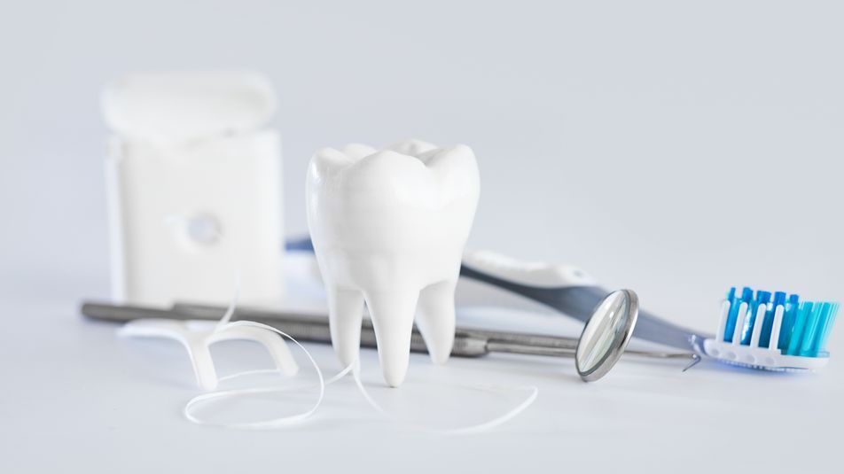 A tooth , toothbrush , floss , mirror and dental instruments on a table.