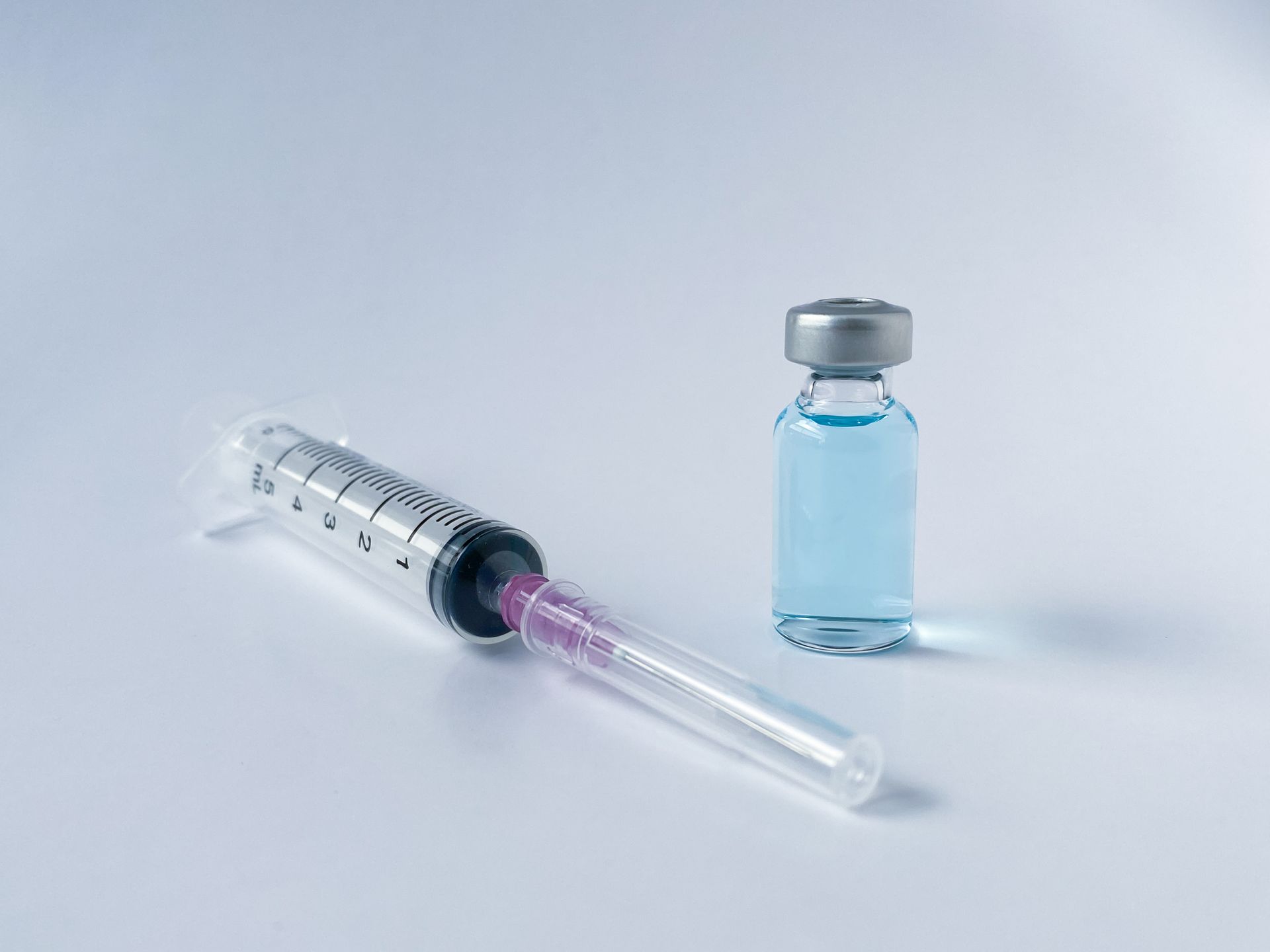 A syringe and a bottle of vaccine on a white surface.
